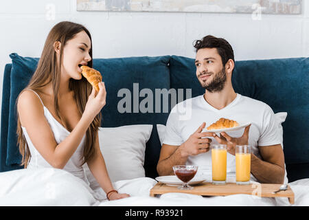 Jeune couple eating délicieux croissants au petit-déjeuner au lit Banque D'Images