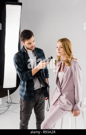 Le jeune photographe holding posemètre et travailler avec modèle féminin en photo studio Banque D'Images