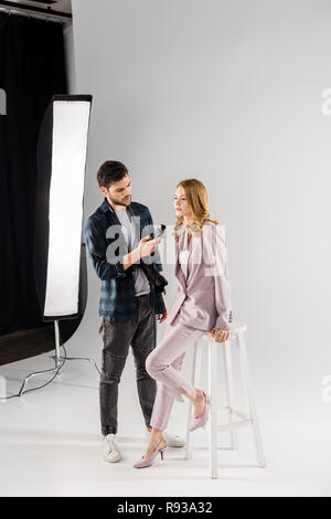 Le jeune photographe holding posemètre et travailler avec de beaux modèle féminin en studio Banque D'Images