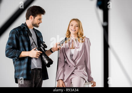 Smiling young photographer holding camera et de posemètre, tout en travaillant avec le modèle en studio Banque D'Images