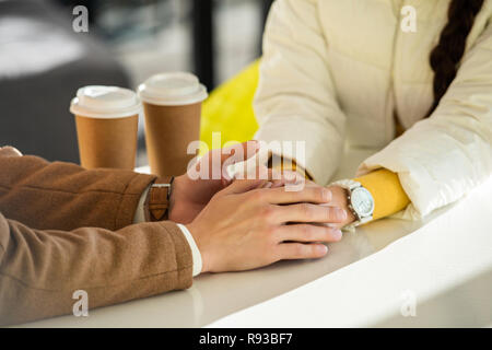 Portrait de l'amour couple holding hands à table avec deux tasses jetables Banque D'Images