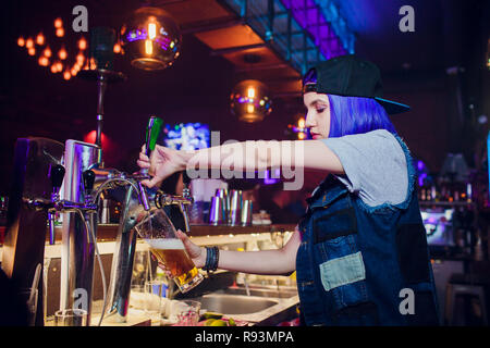 Jeune femme en bar bière distribution de robinets en métal. Belle female bartender touchant la bière dans un bar. Banque D'Images