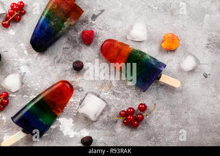 Couleurs arc-en-ciel de la crème glacée à la framboise jaune et rouge, de mûre, de cassis avec popsicle bâton en bois sur fond gris. Vue d'en haut. Arrière-plan de l'alimentation Banque D'Images