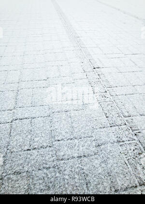 Revêtement carrelage recouvert de première neige. trace de pneu mentions légales sur la surface du trottoir Banque D'Images