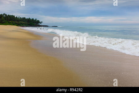 Côte le long de plage de sable fin bordée par des eaux calmes de la mer d'Oman et quelques palmiers et des nageurs sur l'horizon au crépuscule à Thottada, Mumbai. Banque D'Images