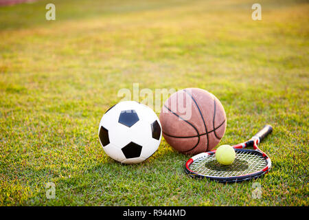 Ballon de soccer de football basket-ball tennis racket portées sur l'herbe au coucher du soleil Banque D'Images