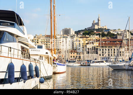 Yachts et voiliers amarrés dans le Vieux Port de Marseille, France, avec la basilique Notre-Dame de la garde en haut de la colline au coucher du soleil. Banque D'Images