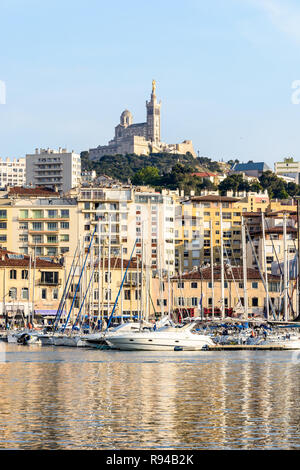 Le Vieux Port de Marseille, France, avec les bateaux et voiliers amarrés dans le port de plaisance et la basilique Notre-Dame de la garde en haut de la colline au coucher du soleil Banque D'Images