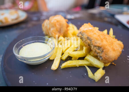 Deux morceaux de poissons panés et frits merlu avec frites et sauce dans un bol en verre plat en noir sur restaurant Banque D'Images