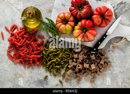 Multicolor pâtes sans gluten avec des ingrédients dont elle est faite sur une table en pierre avec de l'huile d'olive et de tomate brandywine Banque D'Images