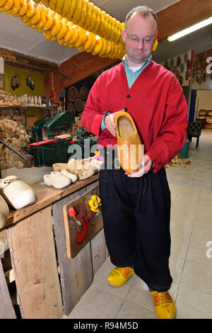 Homme montrant un sabot jaune qu'il vient de faire aux touristes visitant une petite usine à l'extérieur de Volendam, Hollande du Nord, Pays-Bas Banque D'Images