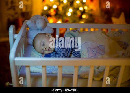 Adorable bébé nouveau-né garçon, dormant dans un lit bébé dans la nuit. Petit garçon au pyjama rayé bleu faire la sieste dans une pièce sombre, la décoration de Noël dans la chambre, Banque D'Images