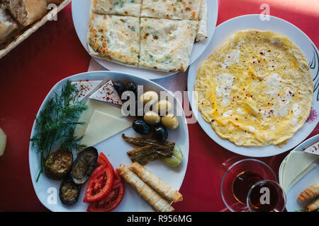 Vue de dessus - omelette, pain, gâteau avec verts, crêpes et assiette de légumes sur la table rouge Banque D'Images