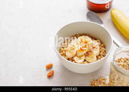 Bol de gruau en céramique blanche avec des tranches de banane et de miel, vu de l'angle élevé en close-up, avec bocal en verre, une cuillère, une banane entière et sur les écrous d'amande Banque D'Images