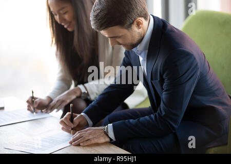 Asian and Caucasian woman sitting at desk signature contr Banque D'Images