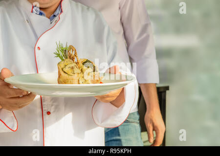 Chef en uniforme portant une plaque avec wrap aux épinards, champignons et fromage fondu et de craquelins Banque D'Images