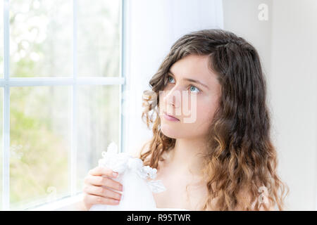 Côté gros plan, portrait de profil de jeunes personne de sexe féminin, femme, mariée en robe de mariage, les cheveux, debout, face à la fenêtre en verre, rideau blanc Banque D'Images