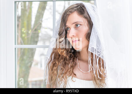 Closeup portrait de jeune femme, femme, mariée en robe de mariée, voile, châle, visage, collier de perle, debout par fenêtre, des rideaux blancs, à la Banque D'Images