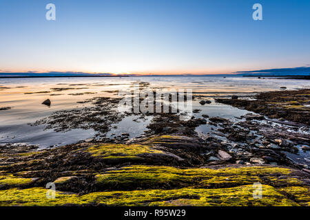 Le coucher du soleil, le crépuscule à Rimouski, au Québec, du fleuve Saint-Laurent, de la Gaspésie, le Canada avec des pierres, rochers, plage de rochers, l'eau turquoise, le soleil au-dessus de la réflexion hori Banque D'Images