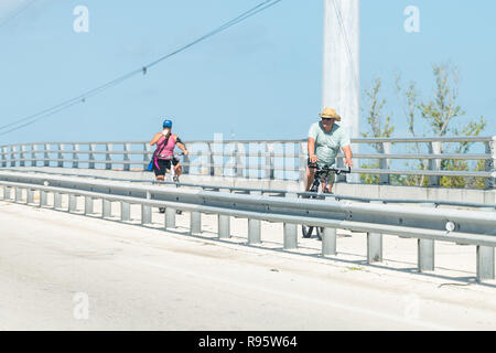 Marathon, USA - 1 mai 2018 : Femme, Homme, couple riding bikes par Overseas Highway, la route US 1, US1 en été, par temps chaud, l'eau potable à partir du bot femelle Banque D'Images