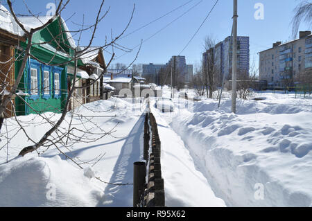 Kovrov, la Russie. 27 mars 2013. Vieilles maisons en bois à un étage avec jardin et vue sur rue avec des bâtiments à plusieurs étages dans l'ensoleillée d Banque D'Images