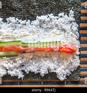 Faire de rouleaux de sushi : Poisson Saumon Concombre, bâtons, fromage à la crème, riz et feuille d'algue Nori sur un tapis de bambou Banque D'Images