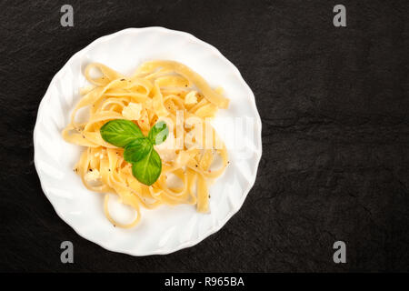 Un plat de pâtes italiennes de fromage Parmesan et feuilles de basilic frais, tourné par le haut sur un fond noir avec copie espace Banque D'Images