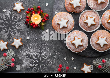 Vue du dessus de la planche de bois avec du sucre saupoudré de muffins, fondants dégivrage et l'étoile de Noël cookies sur fond sombre avec une bougie Banque D'Images