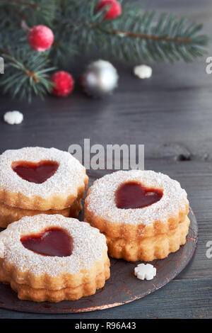 Gros plan sur linzer cookies de Noël traditionnel rempli de confiture rouge sur fond texturé gris avec des décorations de Noël Banque D'Images