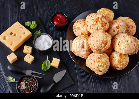 Gougeres au fromage, des balles sur une bouffées plaque noire. Fromage traditionnel français choux buns. fromage et sauce tomate sur une table en bois noir, vue de dessus, Banque D'Images