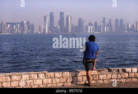 13.09.2010, Doha, Qatar - un homme est la pêche en mer le long de la promenade de la Corniche face à l'horizon de la ville du district commercial central. Banque D'Images