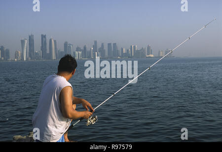 13.09.2010, Doha, Qatar - un homme est la pêche en mer le long de la promenade de la Corniche face à l'horizon de la ville du district commercial central. Banque D'Images