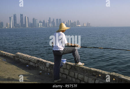 13.09.2010, Doha, Qatar - un homme est la pêche en mer le long de la promenade de la Corniche face à l'horizon de la ville du district commercial central. Banque D'Images