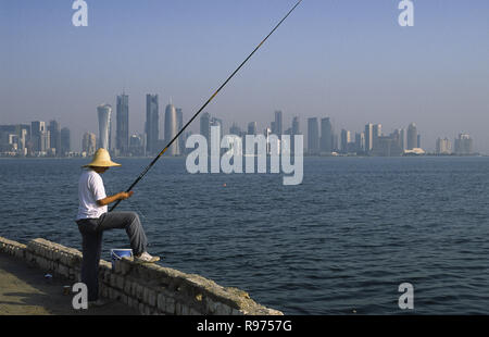 13.09.2010, Doha, Qatar - un homme est la pêche en mer le long de la promenade de la Corniche face à l'horizon de la ville du district commercial central. Banque D'Images