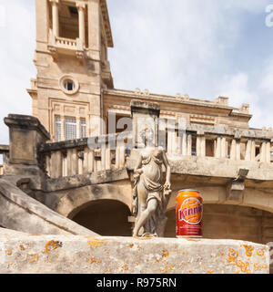 Paceville, à Malte. Se concentrer sur un peut de Kinnie avec un manoir historique et d'une sculpture antique en arrière-plan. Bittersweet maltais boisson brassée à partir d'oranges amères et de l'absinthe. Banque D'Images