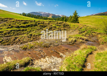 Petit ruisseau en montagne. d'arbres sur la colline au-dessus de l'eau. crête de montagne aux cimes enneigées au loin. belle journée ensoleillée de printemps Banque D'Images