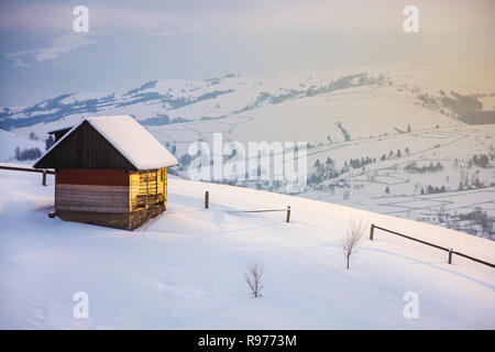 Périphérie du village sur la colline derrière le bûcher. clôture en bois sur une pente enneigée. sommets de la crête de montagne éloignés dans les nuages. merveilleux wint Banque D'Images