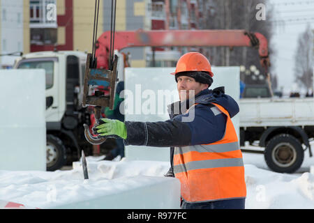 Portrait d'un ajusteur slinger dans un casque et gilet orange sur le déchargement des plaques de glace Banque D'Images