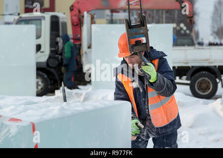 Portrait d'un ajusteur slinger dans un casque et gilet orange sur le déchargement des plaques de glace Banque D'Images
