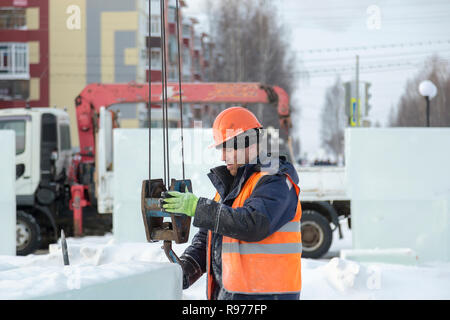 Portrait d'un ajusteur slinger dans un casque et gilet orange sur le déchargement des plaques de glace Banque D'Images