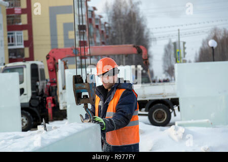 Portrait d'un ajusteur slinger dans un casque et gilet orange sur le déchargement des plaques de glace Banque D'Images