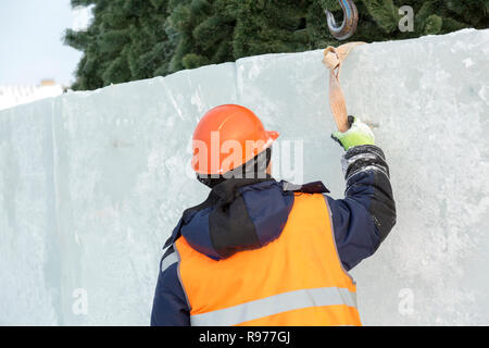 Portrait d'un ajusteur slinger dans un casque et gilet orange sur le déchargement des plaques de glace Banque D'Images