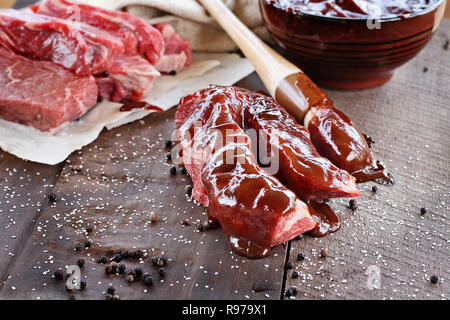 Côtes du pays avec la sauce barbecue et pinceau sur une table rustique. Banque D'Images