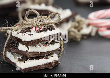 Pile de chocolat blanc et noir de l'écorce de menthe poivrée attachés ensemble avec de la ficelle sur un arrière-plan noir avec plus de bonbons à la menthe dans l'arrière-plan. Ext Banque D'Images