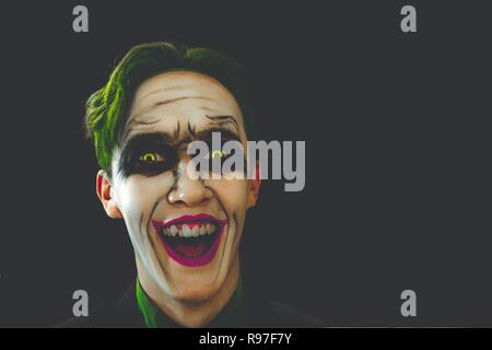 Crazy clown aux cheveux vert, vert et des yeux noirs, chemise verte, le visage blanc et rose lèvres rires dans l'obscurité. Les vacances d'Halloween. L'espace de copie pour le texte Banque D'Images