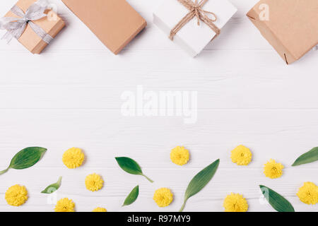 Vue de dessus cadre décoratif fait de coffrets cadeaux sur feuilles vertes et jaunes des boutons de fleurs sur fond de bois blanc, télévision jeter la composition avec fre Banque D'Images
