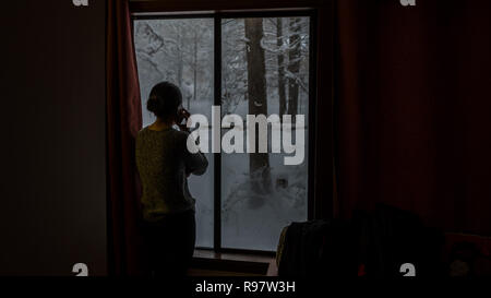 Silhouette de femme parlant au téléphone à fenêtre donnant à la neige Banque D'Images