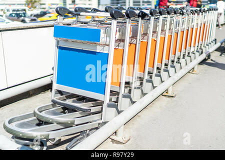 Chariots à bagages bleu et orange dans une rangée à l'extérieur de l'aéroport Banque D'Images