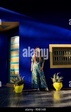 Une dame brune aux cheveux longs portant un citron jaune et bleu robe à motifs de pose sur une terrasse jardin jaune et bleu, éclairé latéralement en plein soleil Banque D'Images