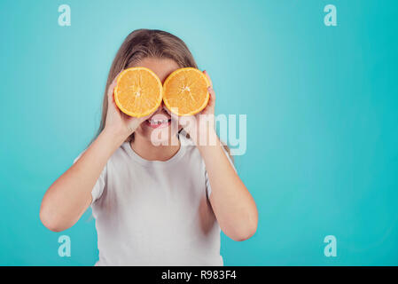 Smiling little girl holding oranges sur ses yeux sur fond bleu Banque D'Images